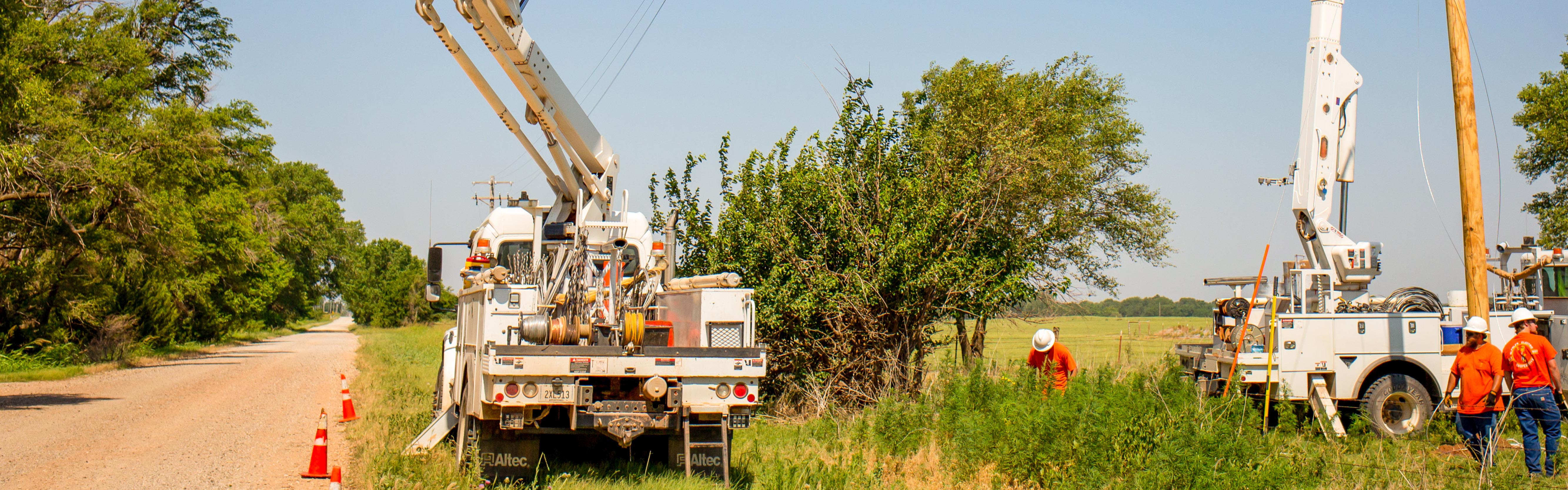 A utility truck is parked along a county road as lineman use the bucket attached to the truck to adjust power lines.