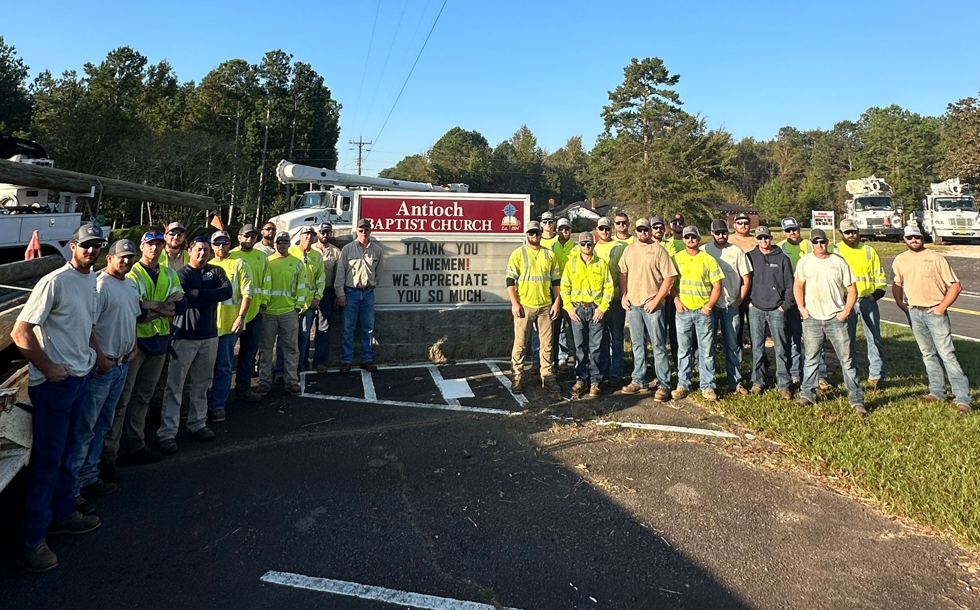 Kansas electric cooperative lineman stand in front of a sign thanking them for helping with power restoration following Hurricane Helen
