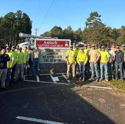 Kansas electric cooperative lineman stand in front of a sign thanking them for helping with power restoration following Hurricane Helen